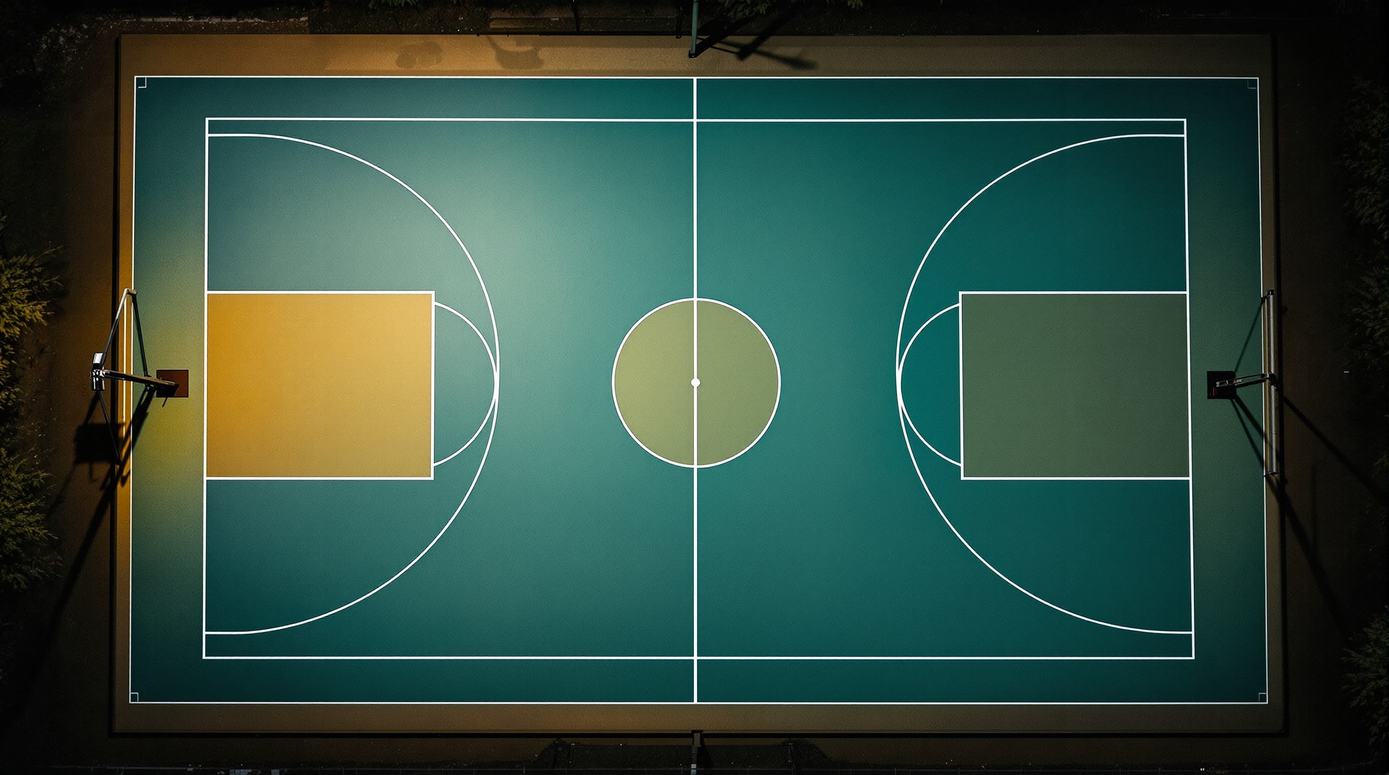 Overhead view of an empty floodlit outdoor basketball court at night