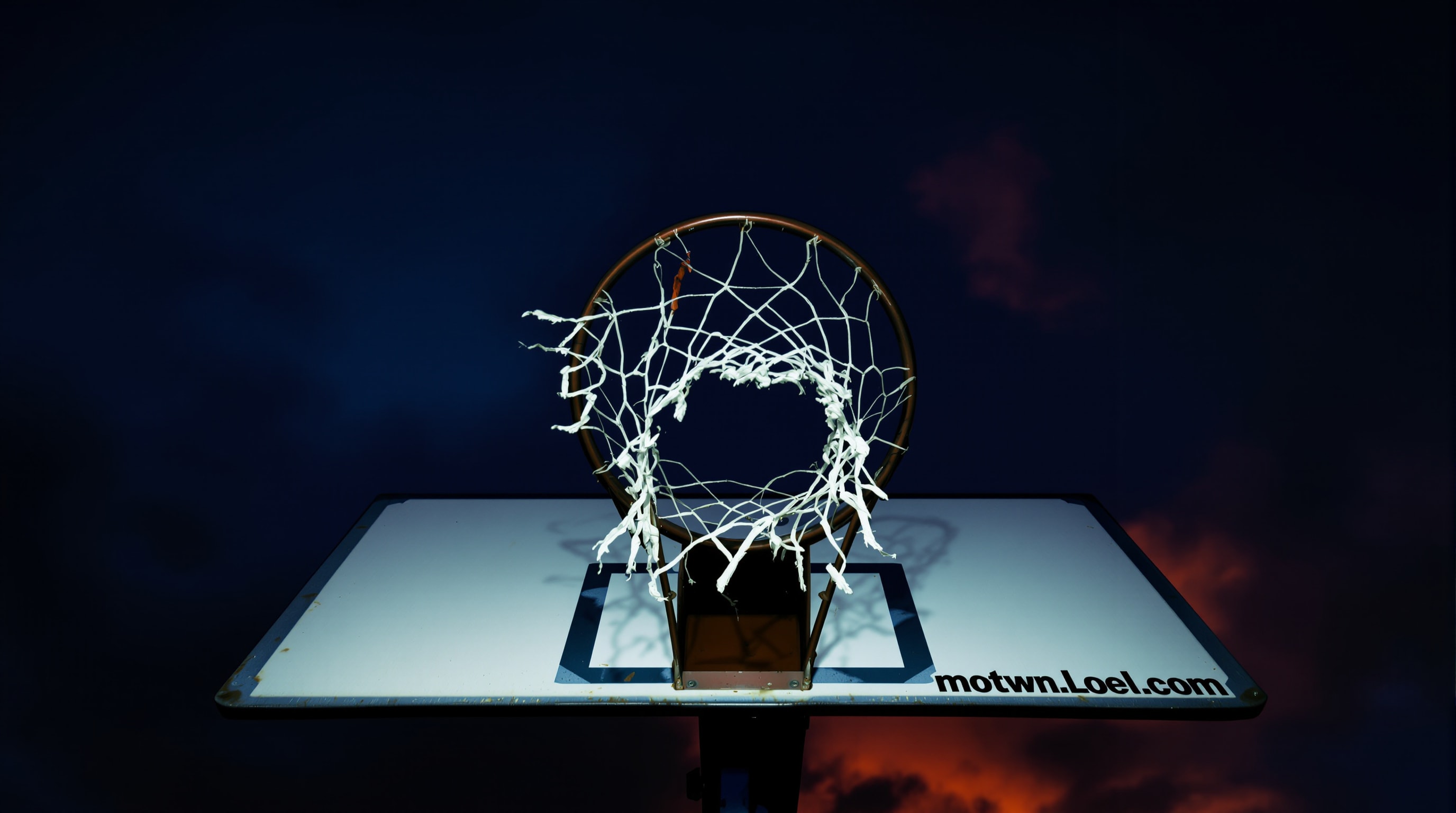 A weathered outdoor basketball hoop silhouetted against a dusk sky